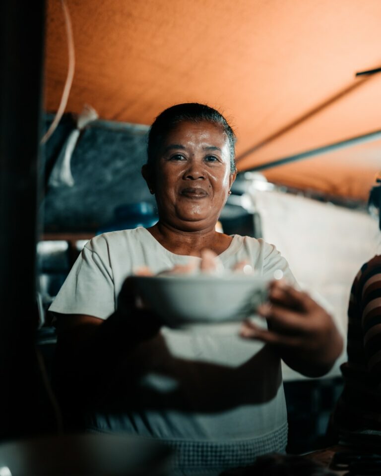 a woman holding a bowl of food under a tent