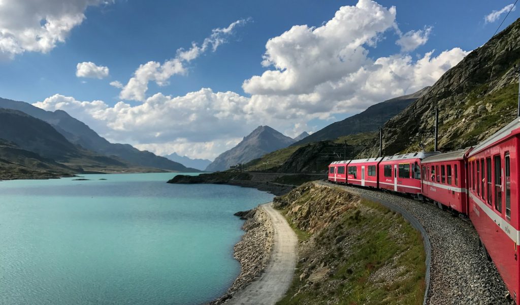 red train travelling near body of water
